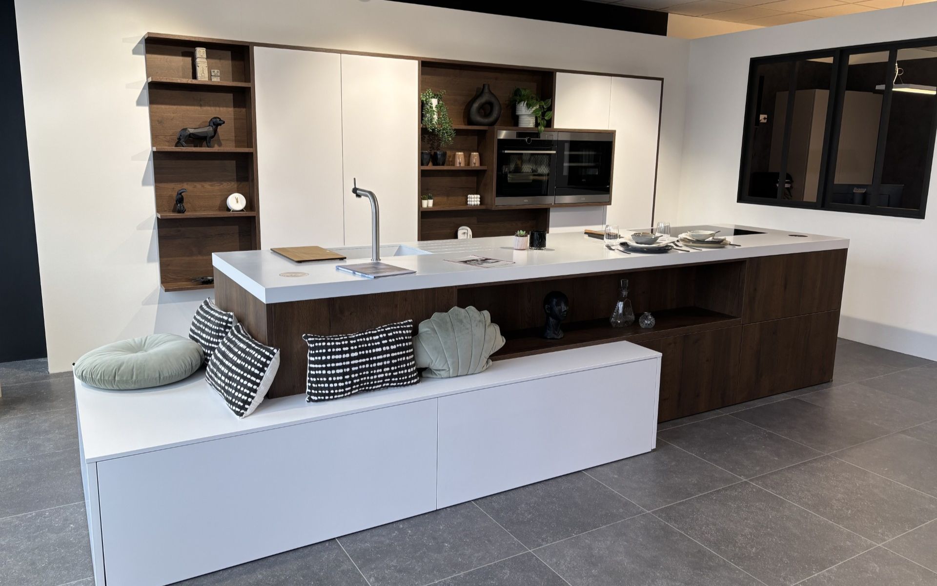 Cuisine équipée d'exposition contemporaine avec îlot central multifonction, assise intégrée et finitions bois et blanc, soldée.