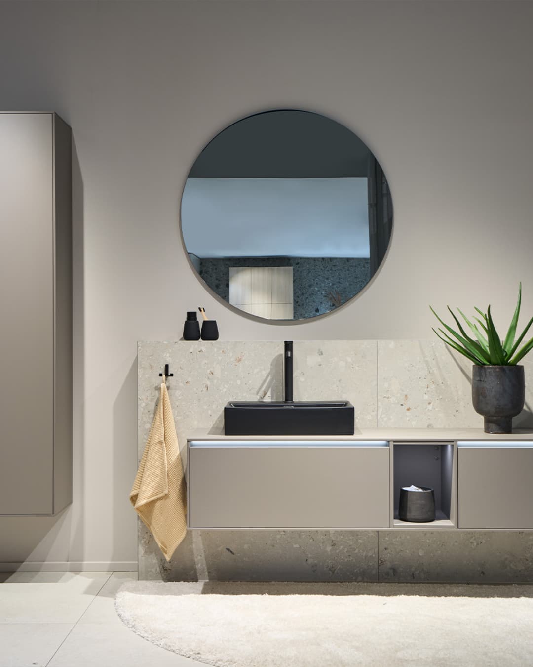 Aménagement de salle de bain avec meuble vasque mural, miroir rond et finitions modernes dans un design épuré et contemporain
