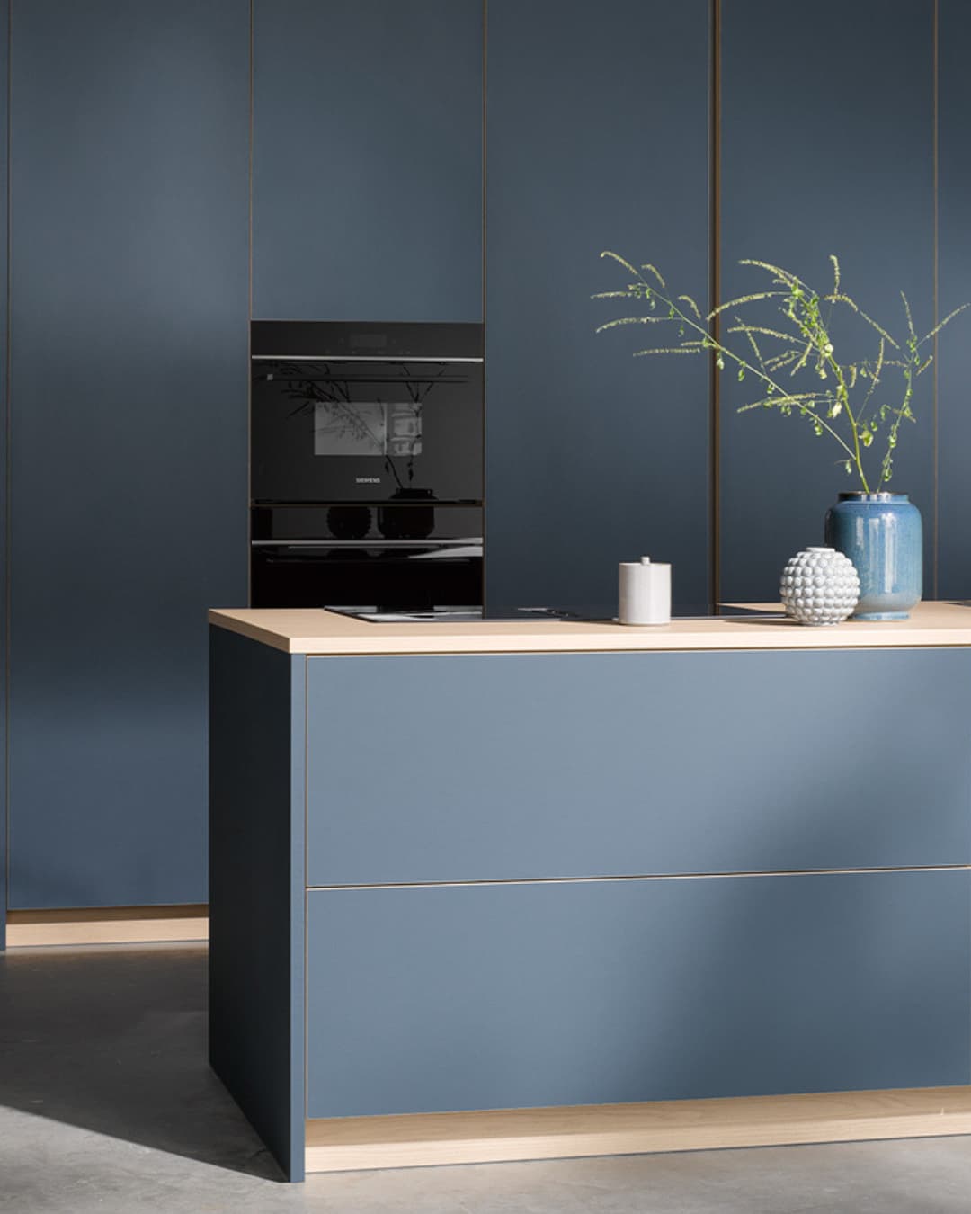 Cuisine contemporaine bleu mat avec îlot assorti et façades toute hauteur jusqu’au plafond, portes grande hauteur au design épuré qui agrandissent visuellement l’espace et dissimulent les colonnes techniques