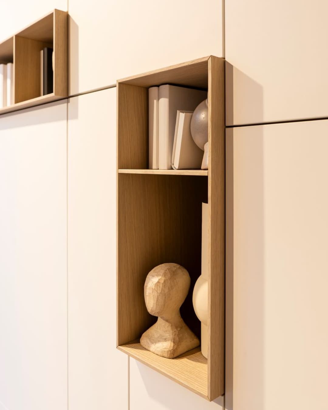 Niche décorative intégrée à un meuble mural sur mesure, finition bois clair et blanc mat, avec objets design et livres