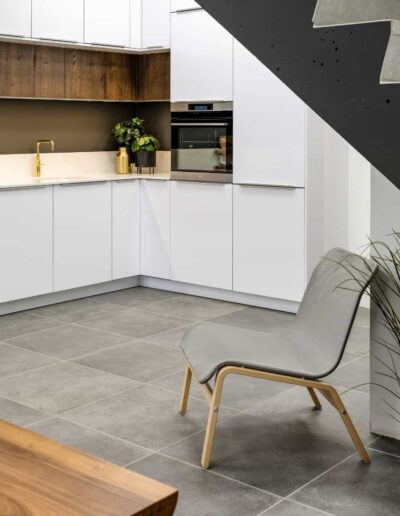 Cuisine blanche sur mesure aménagée avec meubles laqués, plan de travail clair, robinetterie dorée et électroménagers encastrés. Showroom IDEO à Rochefort près de Marche-en-Famenne