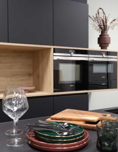 Cuisine équipée design noire et bois avec fours encastrés chez le cuisiniste IDEO à Bastogne
