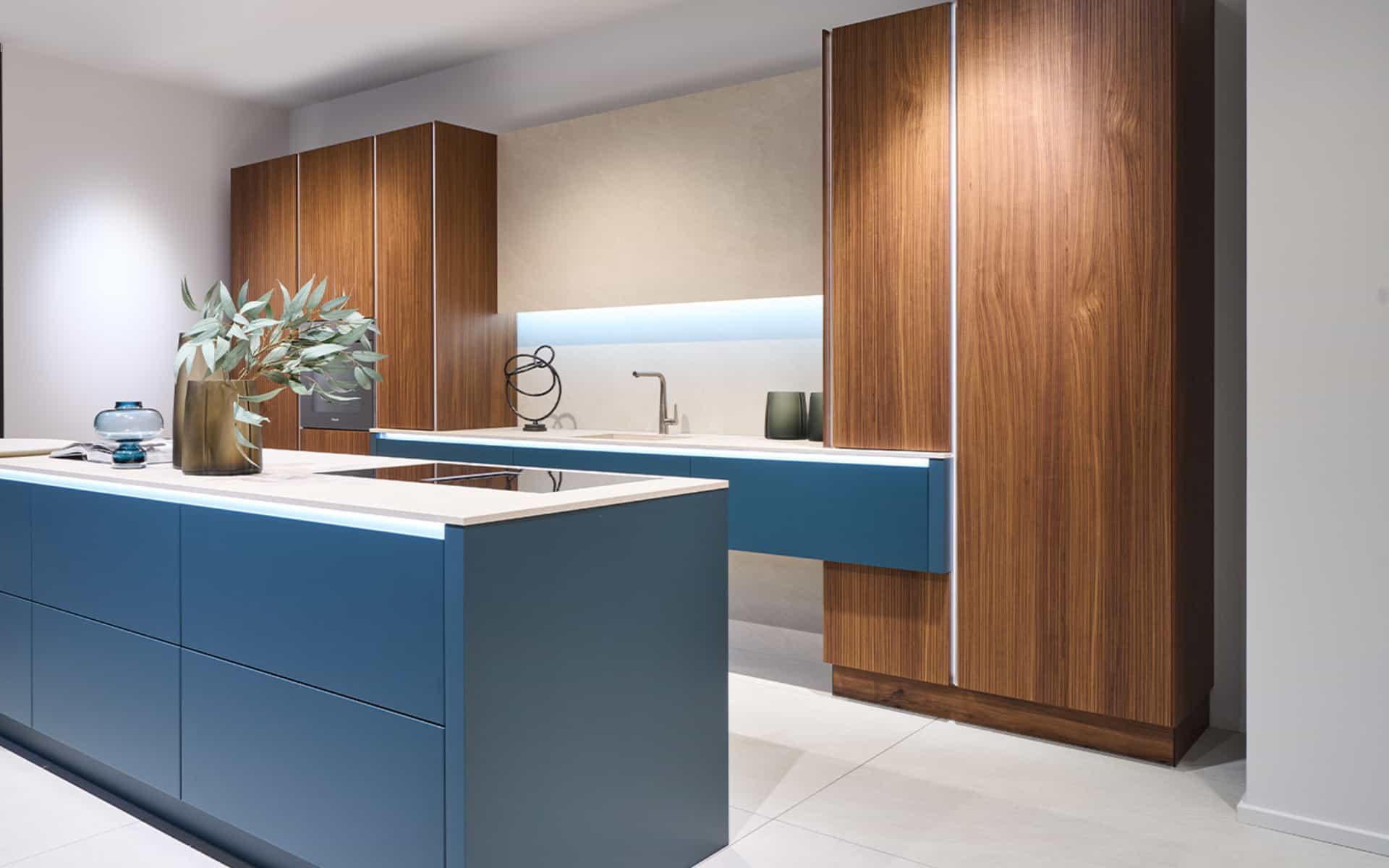 Cuisine design sur mesure aux lignes épurées bleu mat et bois noyer avec plan de travail en céramique blanche et éclairage LED intégré.